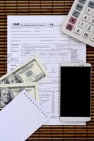 Composition of items lying on the 1040 tax form. Dollar bills, calculator, smartphone, paper clip and notepad. The time to pay taxes photo