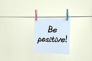 Be positive Note is written on a white sticker that hangs with a clothespin on a rope on a background of beige wall photo