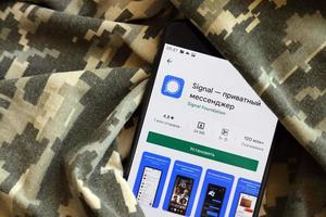 TERNOPIL, UKRAINE - APRIL 24, 2022 Signal Private Messenger app play store page on the display of a black mobile smartphone on ukrainian military camouflage photo