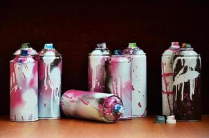 Still life with a large number of used colorful spray cans of aerosol paint lying on the treated wooden surface in the artist's graffiti workshop. Dirty and stained cans for spray art photo