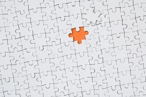 The texture of a white jigsaw puzzle in an assembled state with one missing element forming an orange space photo