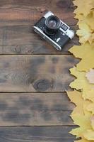 The old camera among a set of yellowing fallen autumn leaves on a background surface of natural wooden boards of dark brown color photo