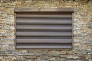 A window with brown metal rolling shutters and wall decoration with artificial stone photo