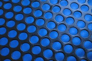 Black metal computer case panel mesh with holes on blue background. Abstract close up image photo