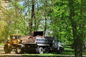 The city improvement team removes the fallen leaves in the park with an excavator and a truck. Regular seasonal work on improving the public places for recreation photo