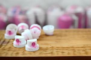 The soiled pink nozzles from the paint sprayer lies on a wooden plank on a background of a many dirty spray cans photo