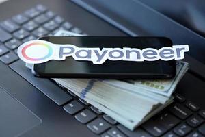 TERNOPIL, UKRAINE - SEPTEMBER 6, 2022 Payoneer paper logotype lies on black laptop with US dollar bills. Payoneer is American financial services company that provides online money transfer photo