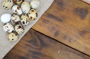 Quail eggs on sacking on a dark brown wooden surface, top view, empty place for text, recipe photo