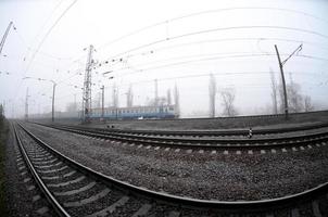 The Ukrainian suburban train rushes along the railway in a misty morning. Fisheye photo with increased distortion