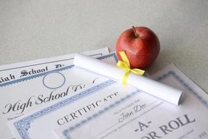 A honor roll recognition, certificate of achievement and high school diploma lies on table with small scroll and red apple. Education documents photo