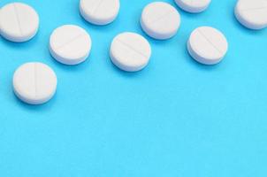 A few white tablets lie on a bright blue background surface. Background image on medical and pharmaceutical topics photo