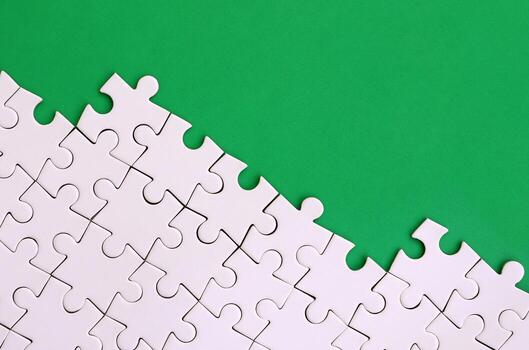 Fragment of a folded white jigsaw puzzle on the background of a green plastic surface. Texture photo with copy space for text