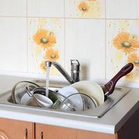 Dirty dishes and unwashed kitchen appliances lie in foam water under a tap from a kitchen faucet photo