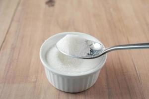 white sugar and spoon in a container on black background, photo