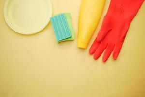 esponja, guantes de goma y plato colorido sobre fondo amarillo foto