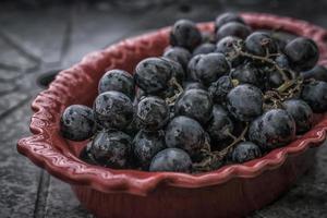 A close-up photo of black grapes in a red bowl