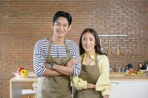 joven pareja asiática sonriente con un delantal en la cocina, concepto de cocina foto