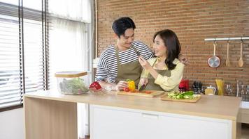 joven pareja asiática sonriente con un delantal en la cocina, concepto de cocina foto