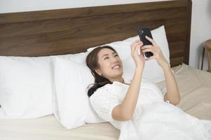 mujer asiática joven que usa el teléfono inteligente antes de acostarse, concepto de estilo de vida feliz foto