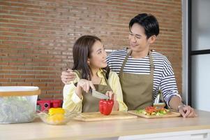 Young smiling asian couple wearing an apron in the kitchen room, cooking concept photo