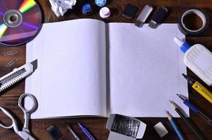 A school or office still life with an open school notebook or checkbook and many office supplies. The school supplies lie on a brown wooden background. Place for text photo