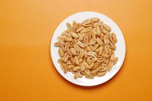 Peeled peanuts on a plate on orange background photo