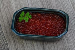 caviar rojo en un recipiente sobre fondo de madera foto