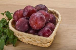 Fresh plums in a basket on wooden background photo