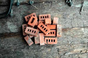 A pile of tiny red bricks lying on an old wooden table photo