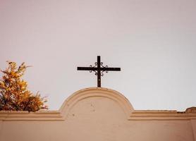 cross on the chapel photographed from below against a background of clear sky and wood photo