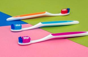 three colored toothbrushes - orange, blue and pink, lying on a colored paper background photo