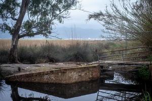 a small old bridge over an irrigation canal among the trees behind which a view of the mountain in the fog photo