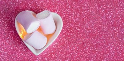 close up photo of three marshmallow in a tiny heart-shaped bowl on a pink glitter background