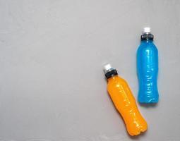 Flat lay shot of two bottles of orange and blue isotonic drink on a grey concrete background with a copy space on a left side photo