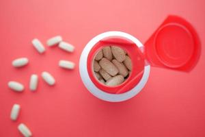 top view of pills spilling from a container on red photo