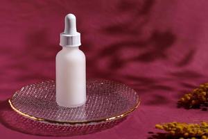 White glass cosmetic bottle on red background with flowers photo