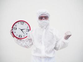 retrato de médico o científico con uniforme de suite ppe sosteniendo un despertador rojo y mirando la cámara con varios gestos. covid-19 concepto aislado fondo blanco foto