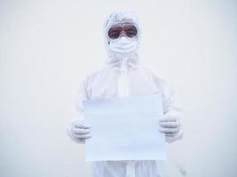 joven médico o científico con uniforme de suite ppe sosteniendo papel en blanco para texto con ambas manos mientras mira hacia adelante. concepto de coronavirus o covid-19 fondo blanco aislado foto