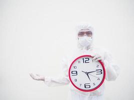 retrato de médico o científico con uniforme de suite ppe sosteniendo un despertador rojo y mirando la cámara con varios gestos. covid-19 concepto aislado fondo blanco foto