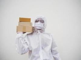 joven con uniforme de suite de ppe mientras sostiene cajas de cartón con guantes médicos de goma y máscara. concepto de coronavirus o covid-19 fondo blanco aislado foto