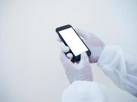Closeup hands of doctor or scientist in PPE suite uniform holding a smart phone with blank white screen for text or design. coronavirus or COVID-19 concept isolated white background photo
