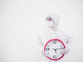 retrato de médico o científico con uniforme de suite ppe sosteniendo un despertador rojo y mirando a la derecha en varios gestos. covid-19 concepto aislado fondo blanco foto