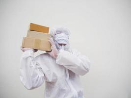 joven con uniforme de suite de ppe mientras sostiene cajas de cartón con guantes médicos de goma y máscara. concepto de coronavirus o covid-19 fondo blanco aislado foto