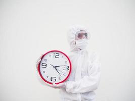 retrato de médico o científico con uniforme de suite ppe sosteniendo un despertador rojo y mirando a la izquierda en varios gestos. covid-19 concepto aislado fondo blanco foto