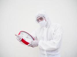 retrato de médico o científico con uniforme de suite ppe sosteniendo un despertador rojo y mirando la cámara con varios gestos. covid-19 concepto aislado fondo blanco foto