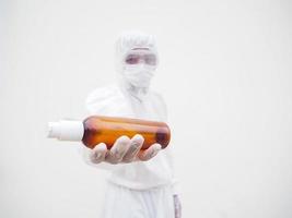 retrato de médico o científico con uniforme de suite de ppe sosteniendo una botella de plástico con un producto para el cuidado de la piel. covid-19 concepto aislado fondo blanco foto