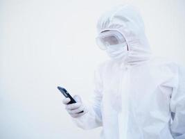 joven médico o científico con uniforme de suite de ppe mientras toca su teléfono para chatear con familiares o amigos. concepto de coronavirus o covid-19 fondo blanco aislado foto