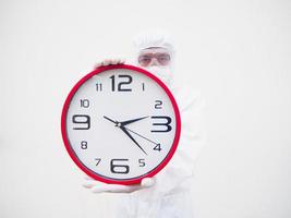 Portrait of doctor or scientist in PPE suite uniform holding red alarm clock and looking at the camera In various gestures. COVID-19 concept isolated white background photo