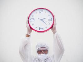 retrato de médico o científico con uniforme de suite ppe sosteniendo un despertador rojo y mirando la cámara con varios gestos. covid-19 concepto aislado fondo blanco foto