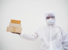 joven con uniforme de suite de ppe mientras sostiene cajas de cartón con guantes médicos de goma y máscara. concepto de coronavirus o covid-19 fondo blanco aislado foto